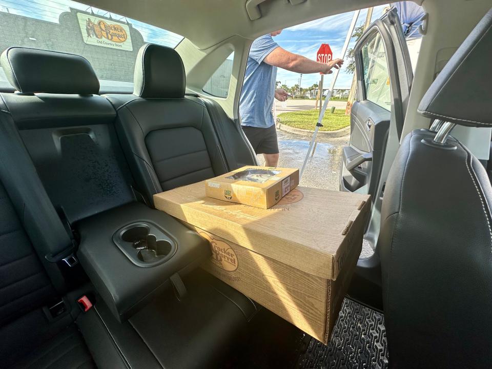 Large Cracker Barrel box with smaller box on top in backseat of a car as man closes car door