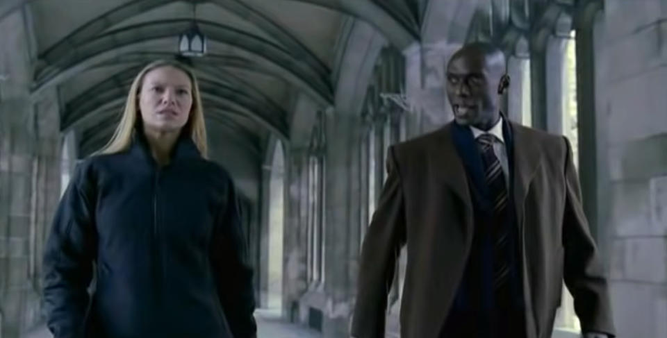 Anna Torv and Lance Reddick walk in a Gothic-style corridor, dressed in formal attire, in a scene from a TV show