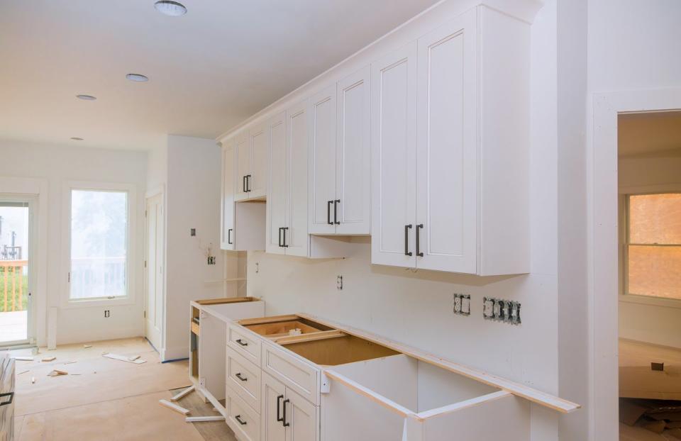 Kitchen in mid-renovation with new white cabinets but a missing countertop and sink