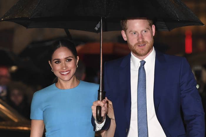 Meghan smiles while Harry holds an umbrella over her