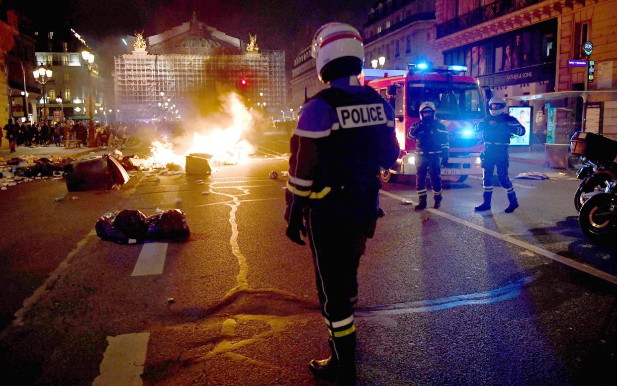 A policeman stands next to a burning pile of rubbish in front of Opera Garnier