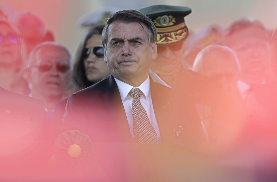 With the red plumes of the helmets of the honor guard in the foreground, wldBrazils President Jair Bolsonaro attends during a military ceremony for the Day of the Soldier, at Army Headquarters in Brasilia, Brazil, Friday, Aug. 23, 2019. Brazilian President Jair Bolsonaro says he's leaning toward sending the army to help fight Amazon fires that have alarmed people across the globe. (AP Photo/Eraldo Peres)