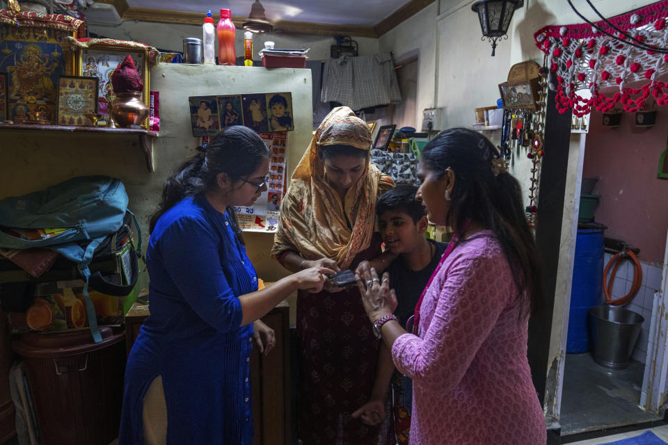 Tanvi Divate, co-founder and Research Manager of Myna Mahila Foundation, left, teaches 32-year-old Komal Vilas Thatkare, center, to use a chatbot powered by artificial intelligence developed by the foundation at her home in Mumbai, India, Feb. 1, 2024. The chatbot, currently a pilot project, represents what many hope will be part of the impact of AI on health care around the globe: to deliver accurate medical information in personalized responses that can reach many more people than in-person clinics or trained medical workers. (AP Photo/Rafiq Maqbool)