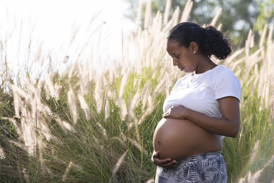 A pregnant woman standing in a meadow of tall green grass. (Getty Images)