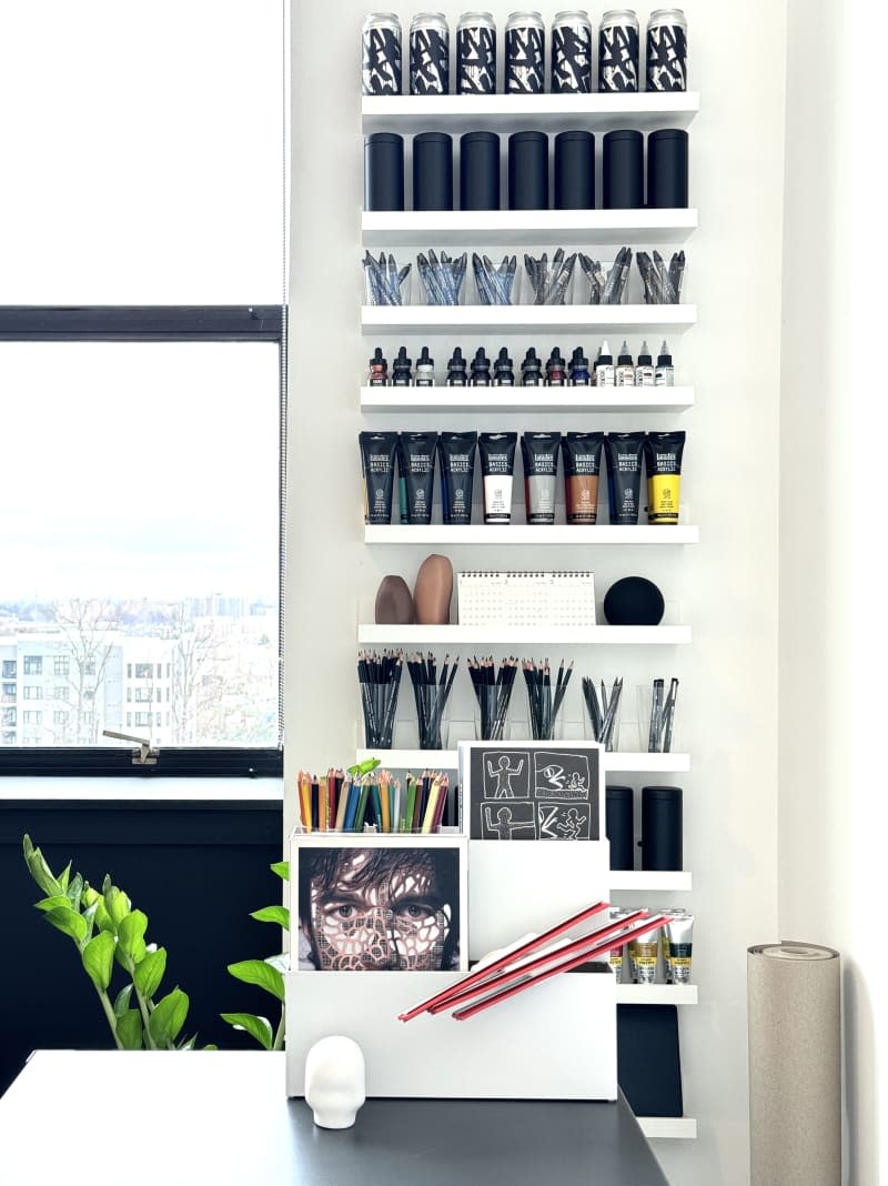 Studio space with art supplies on shelves near a window.