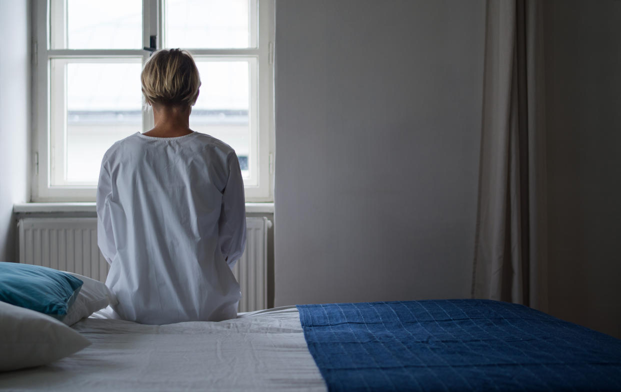 Rear view of woman patient sitting on bed in a hospital.