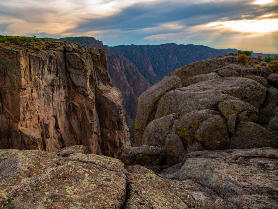 brown craggy cliffs stretch down into a winding canyon with the sun setting behind clouds