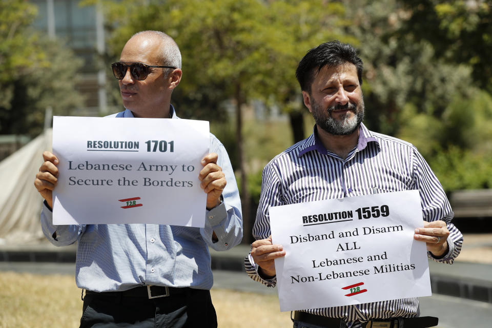 FILE - In this July 24, 2020 file photo, anti-Hezbollah protesters hold banners with the U.N. Resolution 1559, which called for disarmament all Lebanese and non-Lebanese militias, during a sit-in against Hezbollah and Iran in front the United Nations headquarters, in Beirut, Lebanon. For many, the Iran-backed Hezbollah now stands at the top of Lebanon’s sectarian-based system of power — and so is complicit in the corruption many blame for the port disaster and for driving the country into near bankruptcy. (AP Photo/Hussein Malla, File)