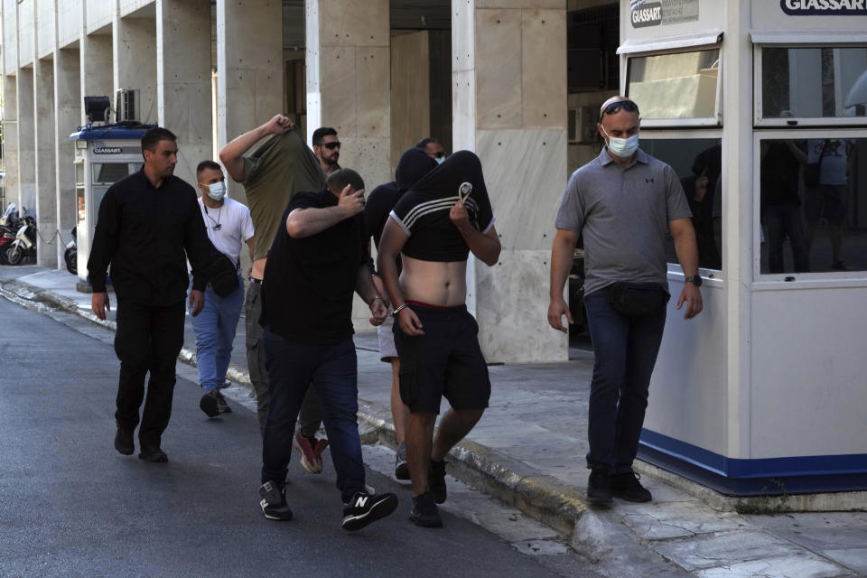 Soccer fans covering their faces, most of them from Croatia, are escorted by police as they leave the Athens Police Headquarters, Greece, Wednesday, Aug. 9, 2023. Ninety-four fans of Croatia's Dinamo Zagreb are appearing in court this morning for a preliminary hearing over Monday night's fan violence that left a fan of Greece's AEK dead and another eight people injured. (AP Photo/Petros Giannakouris)