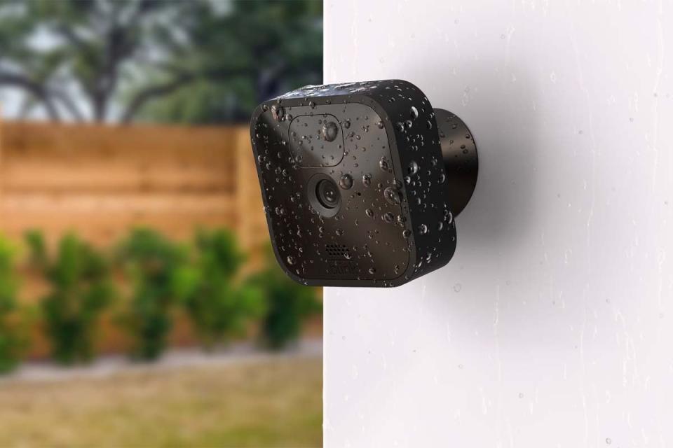 A black security camera is installed on a wall with rain drops on it.