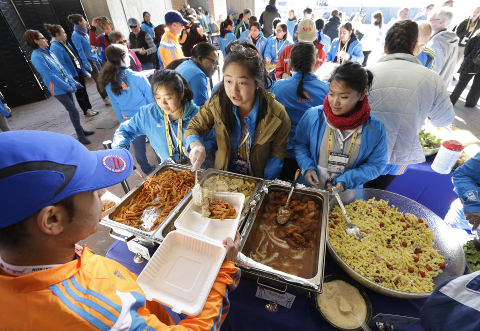 Wellesley College student Tiffany Liao, of San Marino, Calif., center, serves a pasta dish during a Boston Marathon pre-race dinner at Boston City Hall, Sunday, April 20, 2014, in Boston. With an expanded field of runners and the memory of last year's bombings the 2014 Boston Marathon could bring an unprecedented wave of visitors to the area. (AP Photo/Steven Senne)