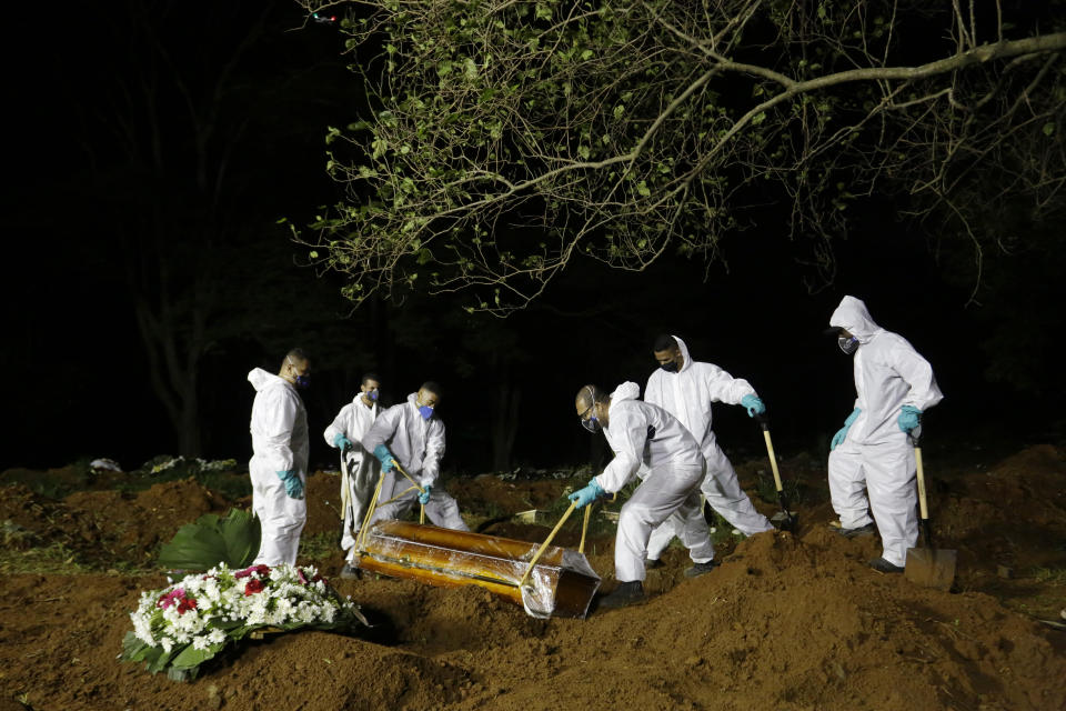 Cemetery workers lower the coffin of a COVID-19 victim into his grave at the Vila Formosa cemetery in Sao Paulo, Brazil, late Wednesday, March 31, 2021. Because of the increased number of deaths in the city, the burial service in some public cemeteries has been extended to the hours of the night. (AP Photo/Nelson Antoine)