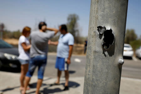 People stand next to a pole damaged by a rocket fired from the Gaza Strip that landed near it, in a Kibbutz on the Israeli side of the Israeli-Gaza border, June 20, 2018. REUTERS/Amir Cohen