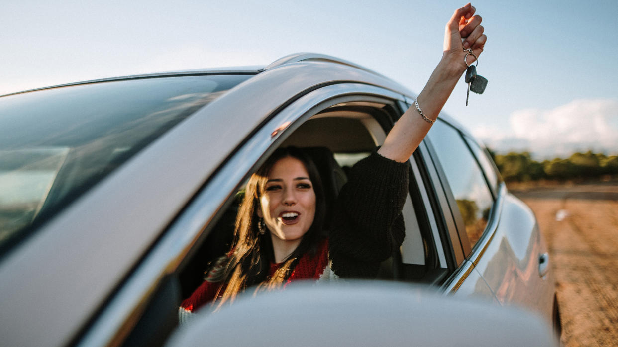 A young woman showing the car keys through the car window.