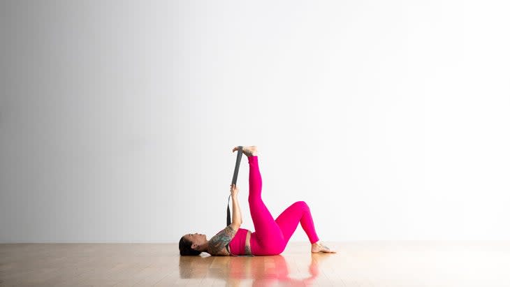 Woman lying on her back with one knee bent and one leg straight and a strap around her lifted leg to stretch her tight hamstrings