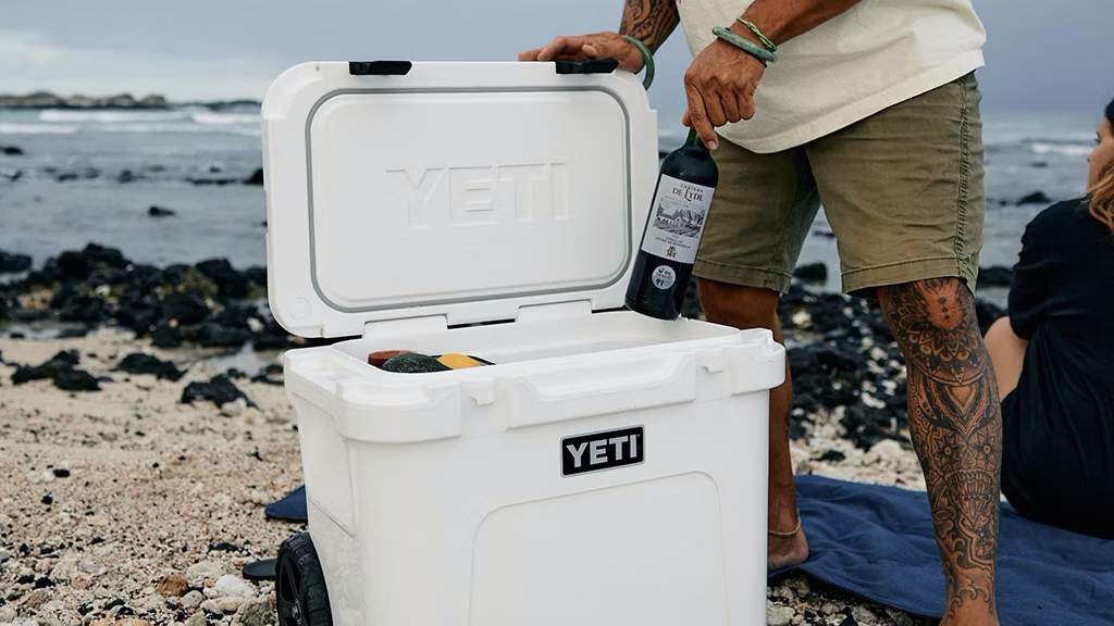  Man taking wine bottle out of Yeti cooler on beach. 