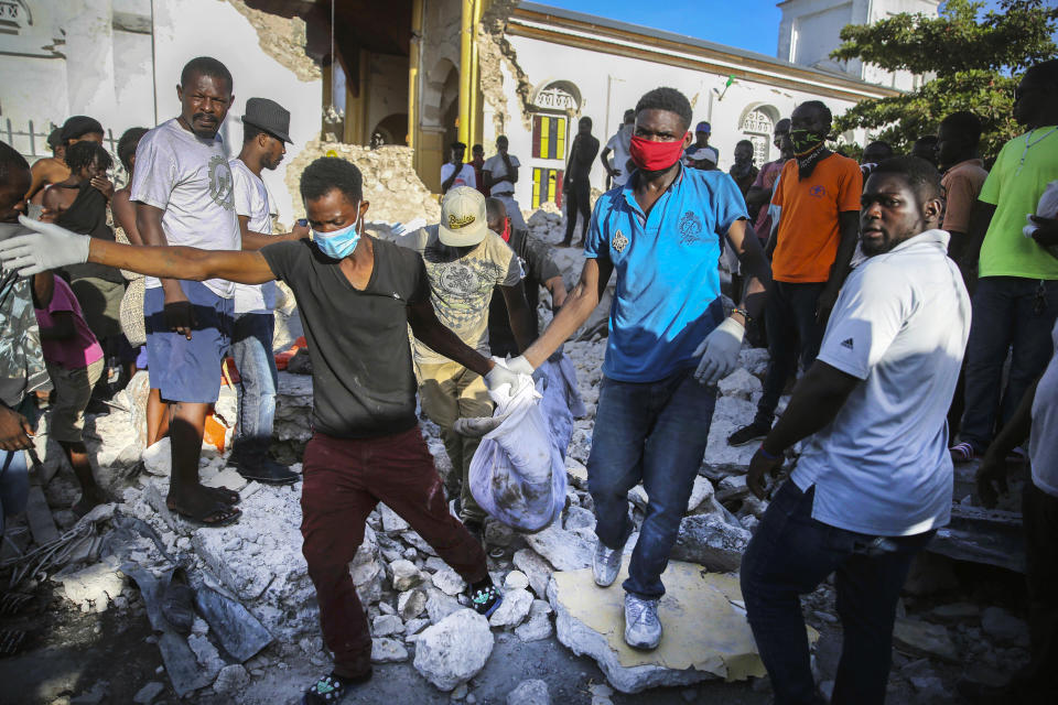 People carry away a body recovered from the rubble of an earthquake destroyed home in Les Cayes, Haiti, Sunday, Aug. 15, 2021. The death toll from a magnitude 7.2 earthquake in Haiti soared to more than 1,200 on Sunday as rescuers raced to find survivors amid the rubble ahead an approaching tropical storm. (AP Photo/Joseph Odelyn)
