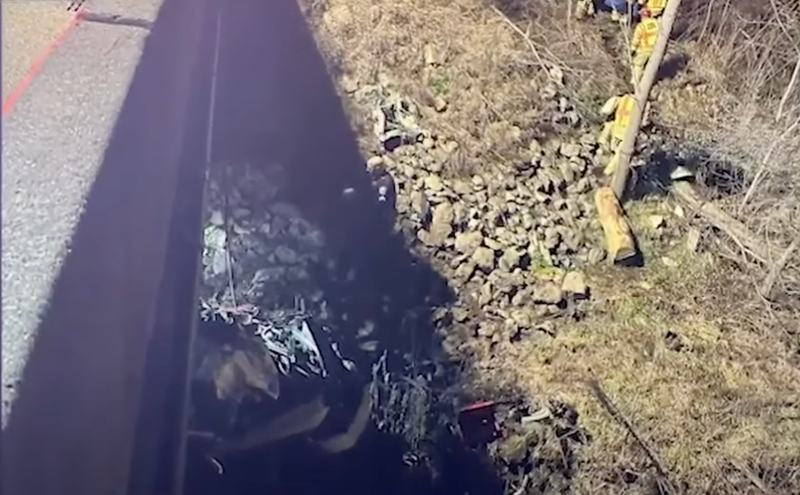 The area under a freeway overpass where a truck lays in crumpled mass among boulders and downed trees