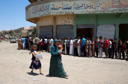 Displaced Iraqi residents carry biscuits and bottles of water as they walk past other residents waiting for the food distribution of an aid organization during the first day of Eid-al Fitr celebration in West Mosul, Iraq June 25, 2017. REUTERS/Erik De Castro