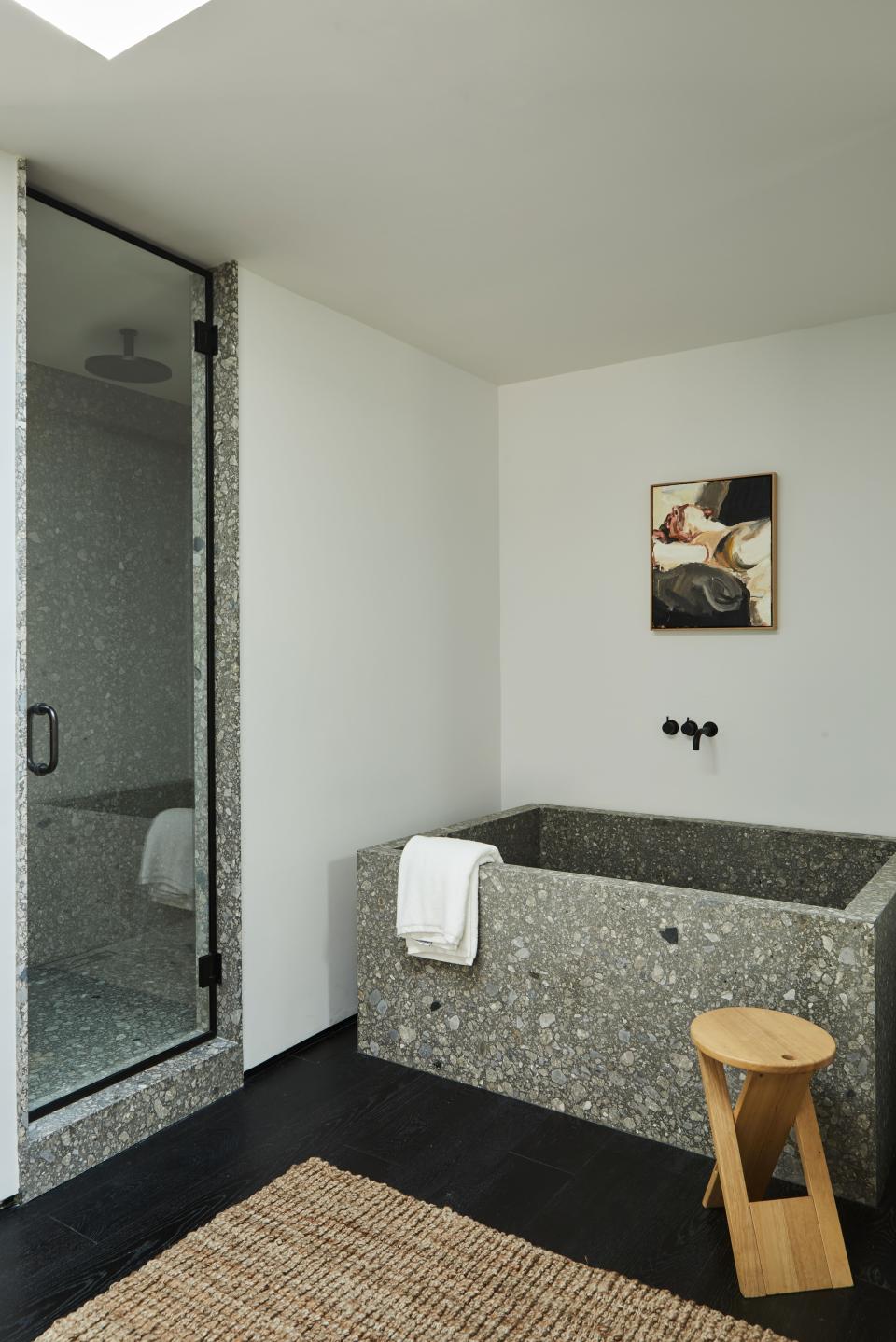 An oil painting by Robert Malherbe from BDDW adorns the wall above the custom tub by OSKLO in extra honed ceppo di gre stone from Stoneland, with Vola tub fittings from EuroConcepts. The Roger Tallon folding stool is from 1stdibs.