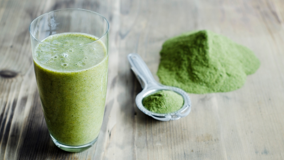 are powdered greens worth it: Moringa powder on spoon and wooden table and glass of moringa smoothie