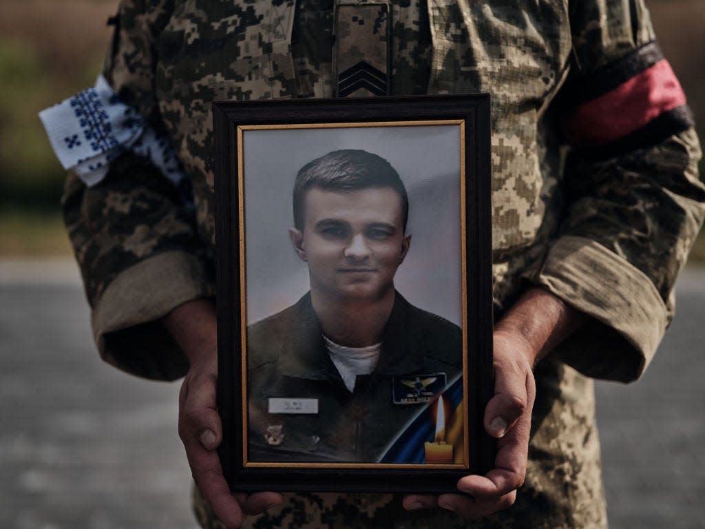 A service member in fatigues holds a picture of a deceased F-16 pilot.