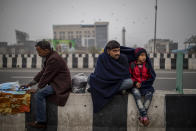 A farmer shares his shawl with a child as they sit on a road divider listening to a speaker during a protest against new farm laws at the Delhi-Uttar Pradesh state border, India, Friday, Jan. 8, 2021. (AP Photo/Altaf Qadri)