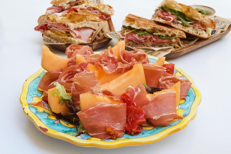 A melon-and-prosciutto salad, with two sandwiches behind it