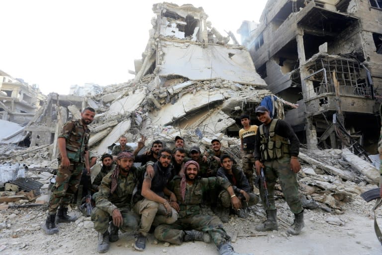 Syrian government forces pose for a photo in front of destroyed buildings at the entrance of the Palestinian camp of Yarmuk on the southern outskirts of Damascus after the army announced it was in complete control of the capital