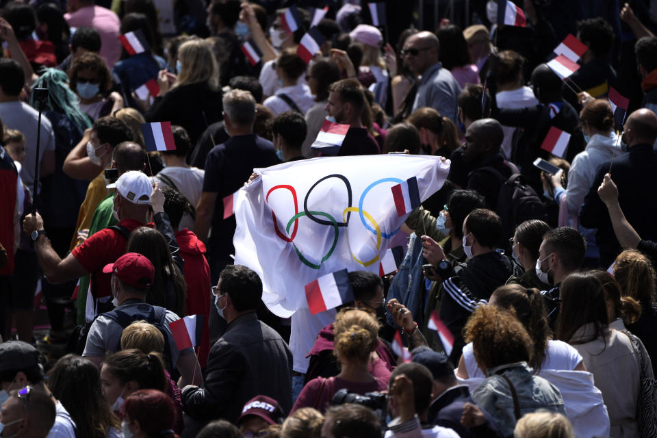 Fans carry a flag in the Olympics fan zone at Trocadero Gardens in front of the Eiffel Tower in Paris, Sunday, Aug. 8, 2021. A giant flag will be unfurled on the Eiffel Tower in Paris Sunday as part of the handover ceremony of Tokyo 2020 to Paris 2024, as Paris will be the next Summer Games host in 2024. The passing of the hosting baton will be split between the Olympic Stadium in Tokyo and a public party and concert in Paris. (AP Photo/Francois Mori)