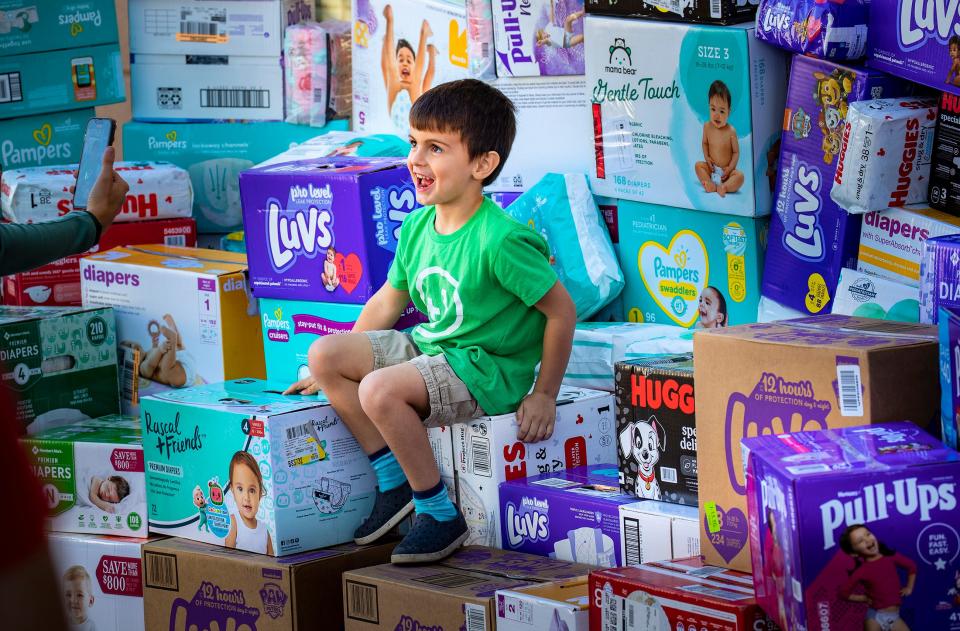 T.J. climbs atop a stack of diapers Thursday afternoon at the One More Child campus in Lakeland. About two dozen employees and volunteers gave the 5-year-old an ovation as he arrived with his parents to donate 162 boxes of diapers.