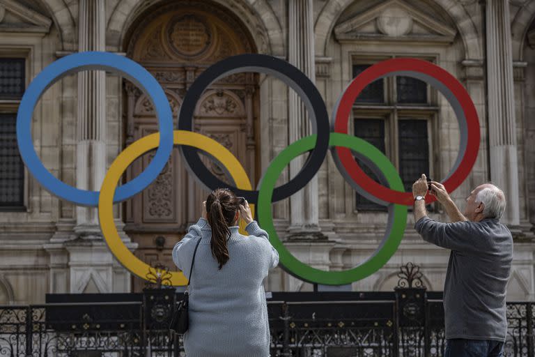 ARCHIVO - Dos personas toman fotos de los anillos olímpicos en el ayuntamiento de París, el 30 de abril de 2023. (AP Foto/Aurelien Morissard)