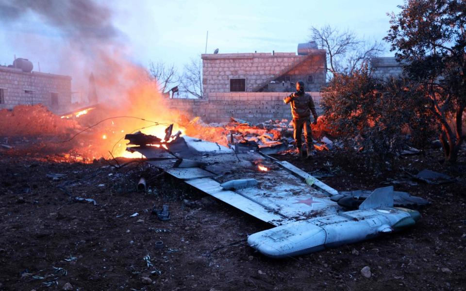 Rebel fighter taking a picture of a downed Sukhoi-25 fighter jet in Syria's northwest province of Idlib. - AFP