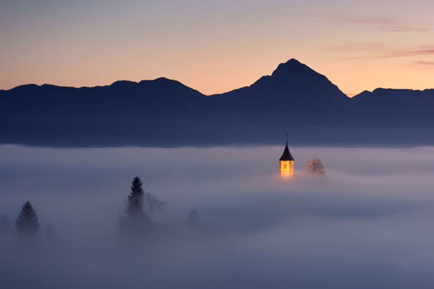 Ein Stück vom Himmel: Dicker Nebel hängt über dem kleinen slowenischen Dorf Jamnik. Nur der beleuchtete Kirchturm ragt aus dem Wattemeer hervor - und Janez Tolar war genau zur richtigen Zeit am richtigen Ort, um diese märchenhafte Morgenstimmung festzuhalten. (Bild: Janez Tolar/Mehr Bilder finden Sie hier: <a href="http://ngm.nationalgeographic.com/ngm/photo-contest/2012/entries/recent-entries/" rel="nofollow noopener" target="_blank" data-ylk="slk:National Geographic Photo Contest;elm:context_link;itc:0;sec:content-canvas" class="link ">National Geographic Photo Contest</a>)