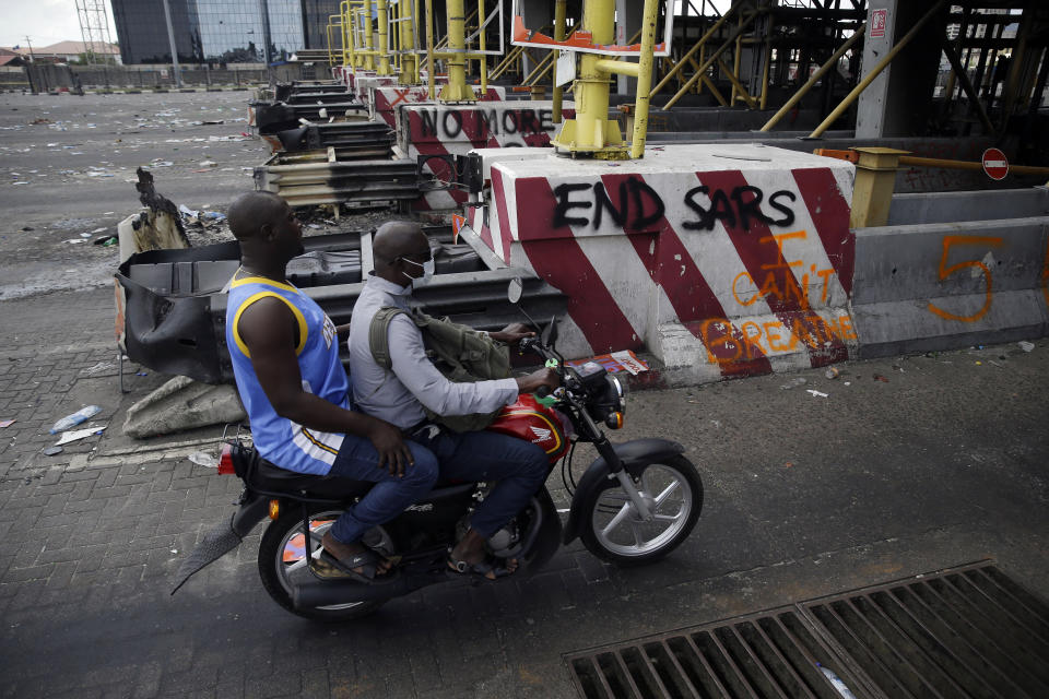 People drive past burnt toll gates with anti police slogans sprayed across, in Lagos Friday, Oct. 23, 2020. Resentment lingered with the smell of charred tires Friday as Nigeria's streets were relatively calm after days of protests over police abuses, while authorities gave little acknowledgement to reports of the military killing at least 12 peaceful demonstrators earlier this week. (AP Photo/Sunday Alamba)