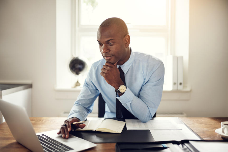 A man sitting at a desk looks at his laptop.