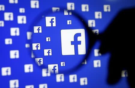 A man poses with a magnifier in front of a Facebook logo on display in this illustration taken in Sarajevo, Bosnia and Herzegovina, December 16, 2015. REUTERS/Dado Ruvic