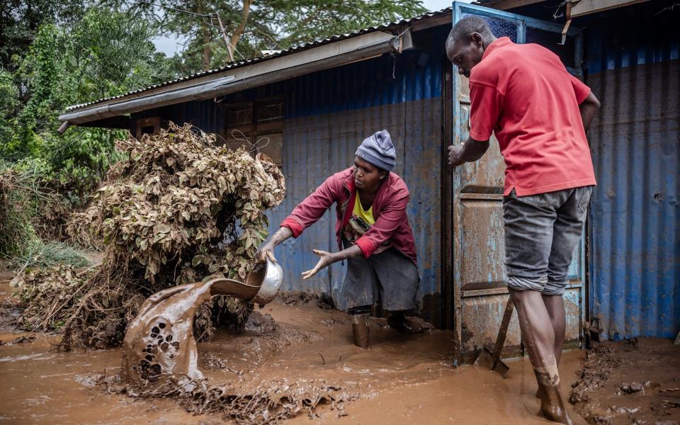 A woman and a man take mud and water out of their house in an area heavily affected by torrential rains and flash floods in Mai Mahiu,