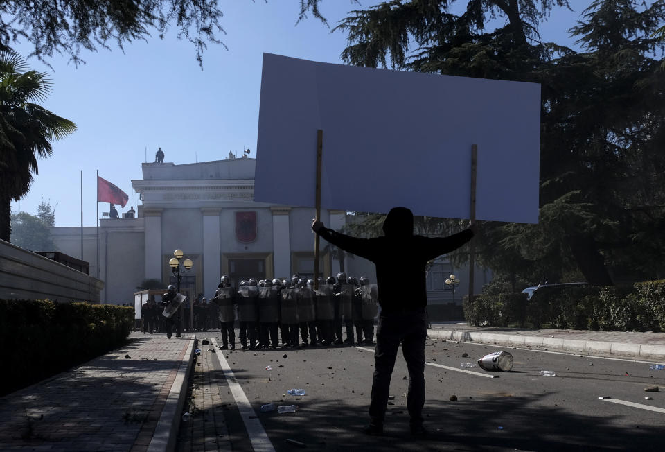 A protester raises a banner in front of a police formation during an anti-government rally in Tirana, Albania, Saturday, March 16, 2019. Albanian opposition supporters clashed with police while trying to storm the parliament building Saturday in a protest against the government which they accuse of being corrupt and linked to organized crime. (AP Photo/Hektor Pustina)