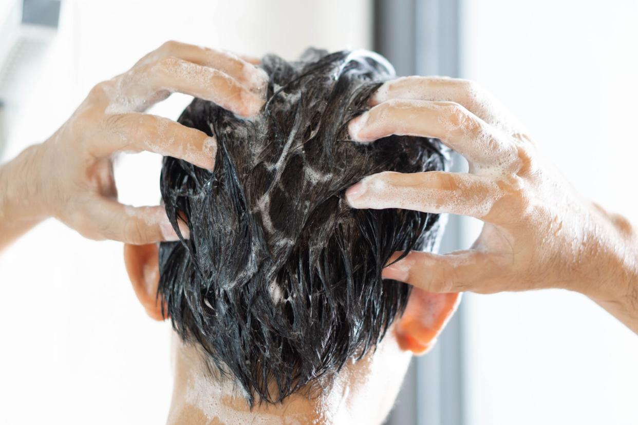 Closeup young man washing hair with with shampoo in the bathroom, vintage tone, selective focus