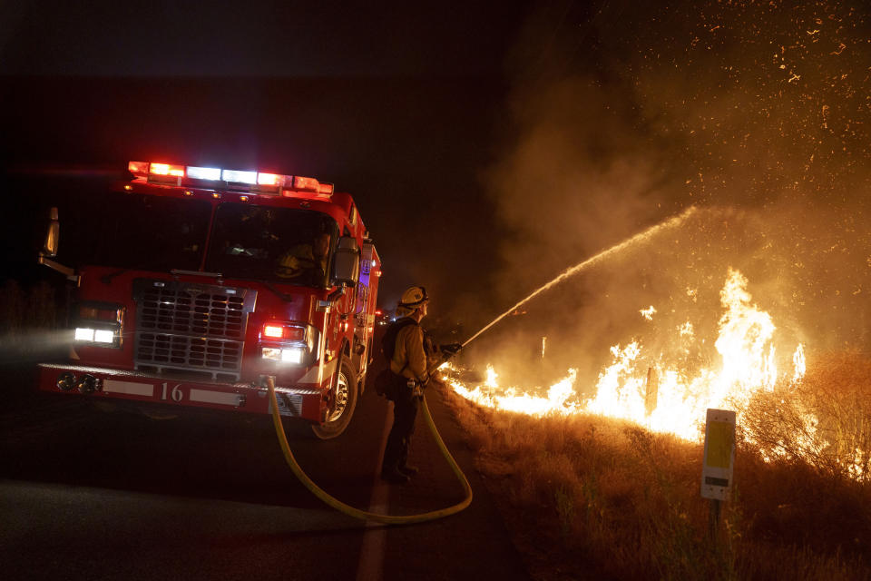 A firefighter sprays water on flames along Gilman Springs Road during the Rabbit Fire late Friday, July 14, 2023, in Moreno Valley, Calif. (AP Photo/Eric Thayer)