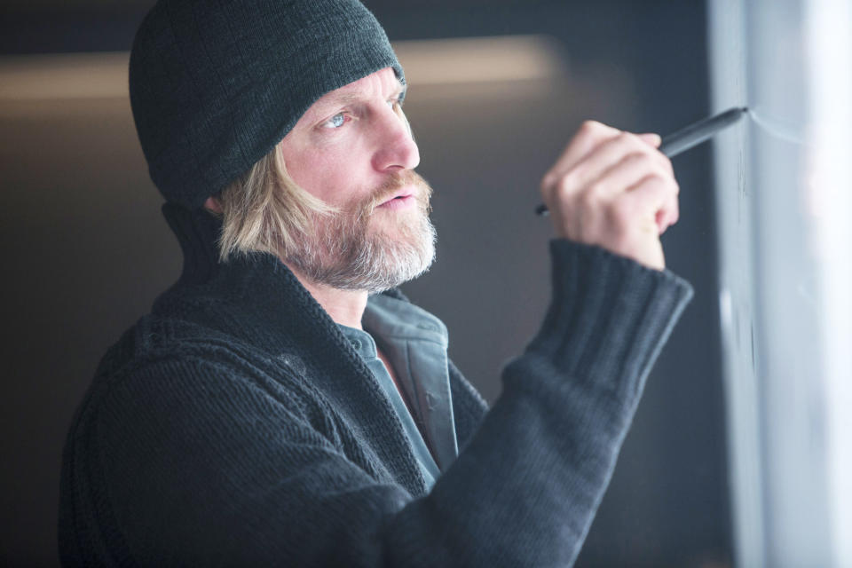 Woody Harrelson writing on a glass board while wearing a knit beanie and a thick sweater