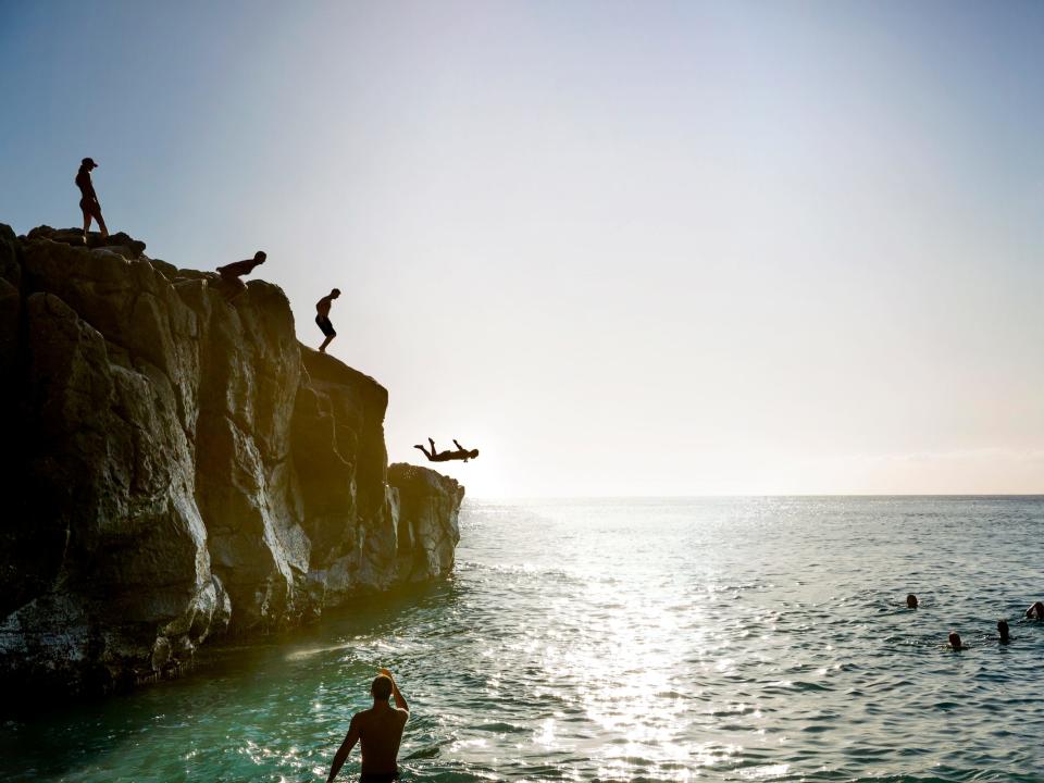People jump from a cliff into the Pacific Ocean at Waimea Bay, North Shore Oahu, Hawaii.