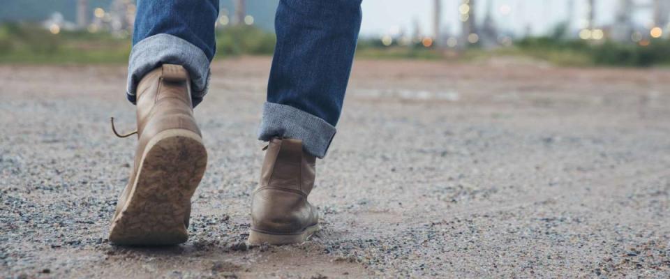 Closeup of leg of engineer or safety officer ,wearing fashion blue jeans. safety brown shoes ,standing in front of a refinery building.