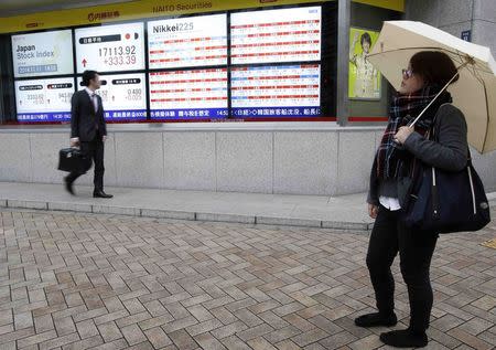 A pedestrian looks at an electronic board showing Japan's Nikkei average (top 2nd from L) and various stock prices outside a brokerage in Tokyo November 11, 2014. REUTERS/Yuya Shino