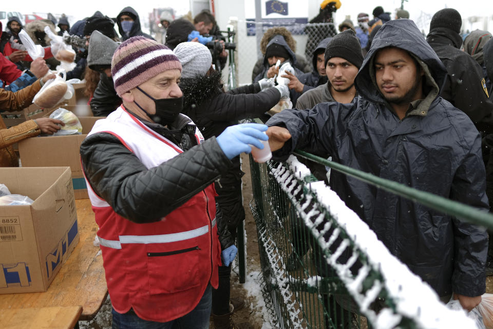 Migrants receive food handouts during a snowfall at the Lipa camp, outside Bihac, Bosnia, Friday, Jan. 8, 2021. A fresh spate of snowy and very cold winter weather on has brought more misery for hundreds of migrants who have been stuck for days in a burnt out camp in northwest Bosnia waiting for heating and other facilities. (AP Photo/Kemal Softic)