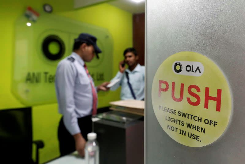 FILE PHOTO: An employee speaks over his phone as a private security guard looks on at the front desk inside the office of Ola cab service in Gurugram