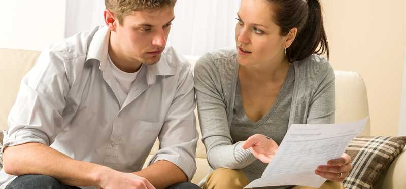 A young couple reviews paperwork while sitting on a couch.