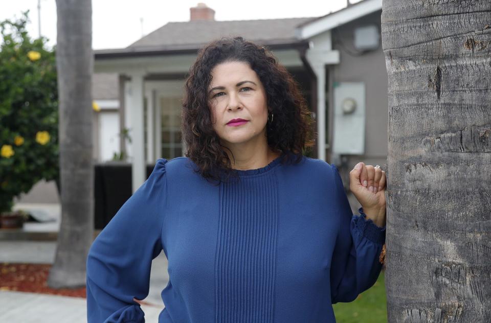 A woman in a blue top leans against a wall