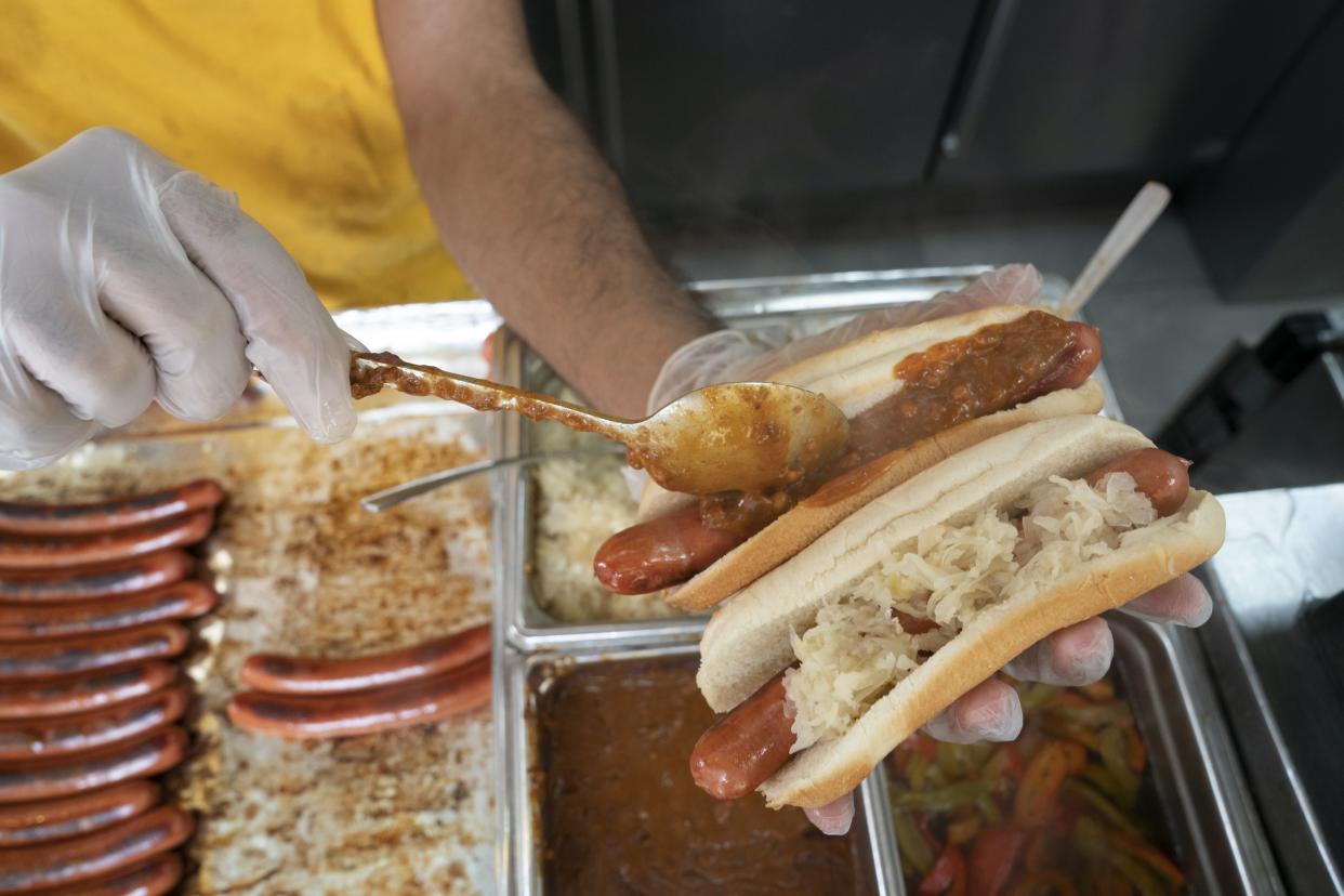 An employee of Papaya King, an Upper East Side staple, tops a hotdog Friday, July 8, 2022 in Manhattan, New York. 